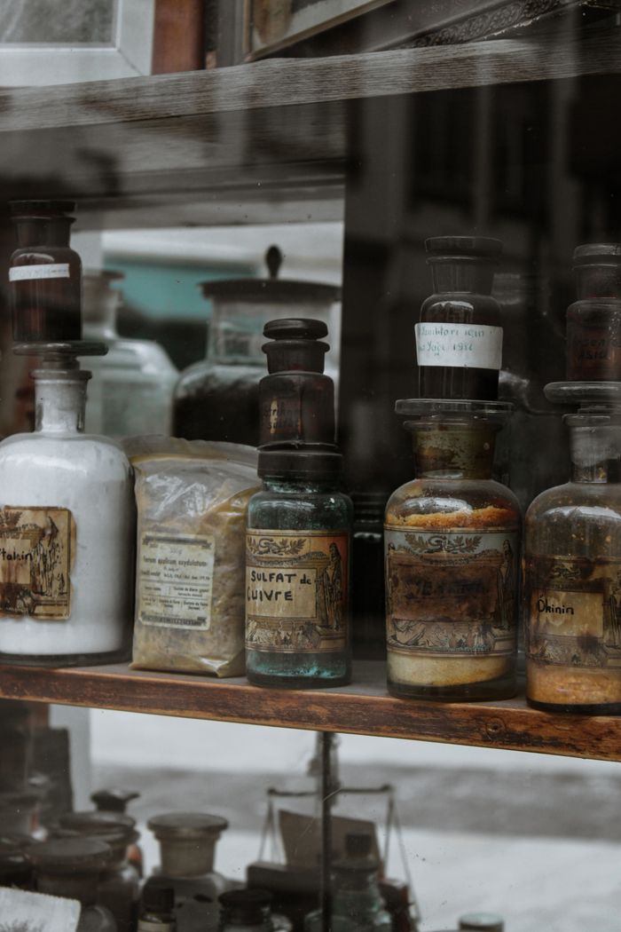 Home A collection of vintage apothecary bottles and jars on a rustic wooden shelf.