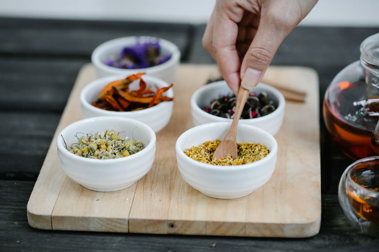 Home Close-up of hand choosing dried spices from bowls on a wooden tray, perfect for culinary themes.